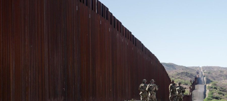 Four members of Arizona Border Recon, a civilian patrol group, walk in the shadow of fencing along the U.S.-Mexico border west of Nogales, Ariz, on Oct. 29, 2023. (Jia Li / Scripps News)